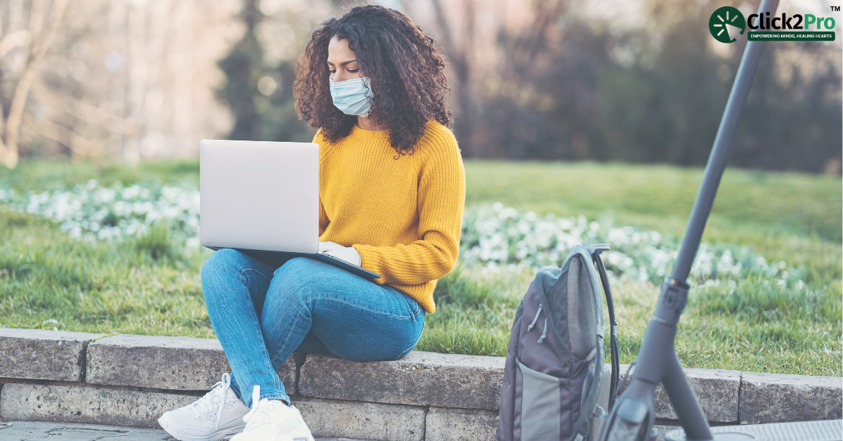 Person wearing a mask using a laptop outdoors, highlighting social isolation and technology connection.