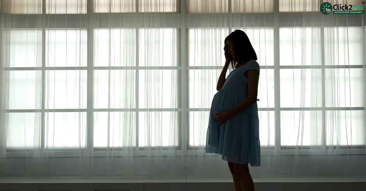 Pregnant woman standing by a window looking stressed, representing stress during pregnancy.