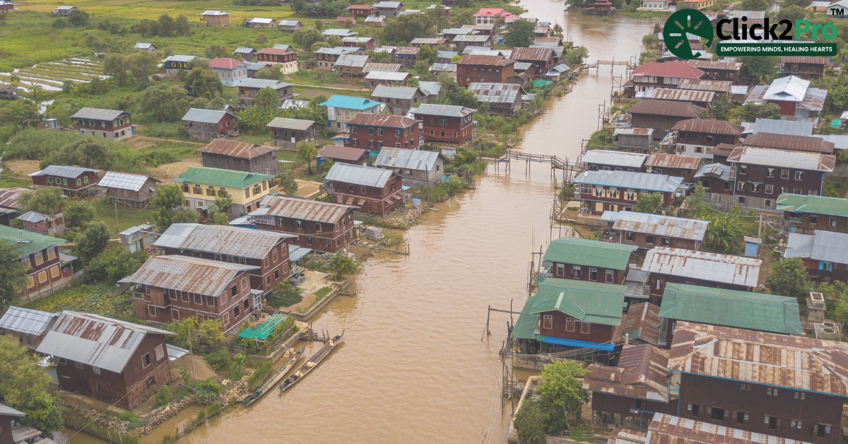 Flooded rural village showing houses along a waterlogged river, highlighting the impact of floods on mental health support in rural areas.