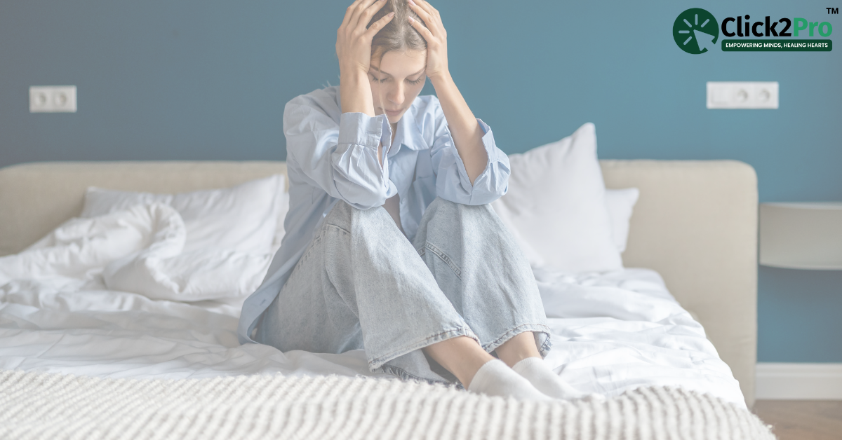 Young woman sitting on bed with head in hands, feeling distressed, representing emotional abuse trauma.